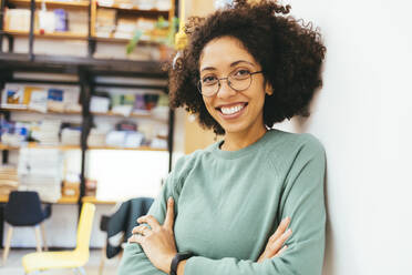 Happy businesswoman with arms crossed in creative office - OYF00666