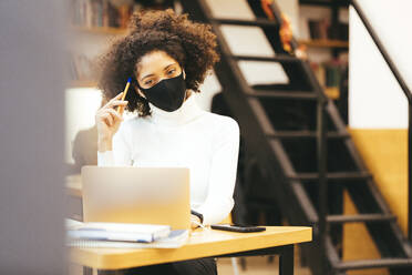 Geschäftsfrau mit Schutzmaske bei der Arbeit am Laptop im Büro - OYF00676