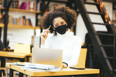 Geschäftsfrau mit Schutzmaske bei der Arbeit am Laptop im Kreativbüro - OYF00677