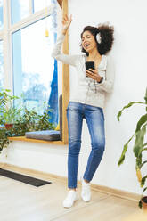 Cheerful woman dancing and listening music through headphones at home - OYF00696