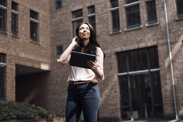Smiling businesswoman with tablet PC standing in front of building - JOSEF06468
