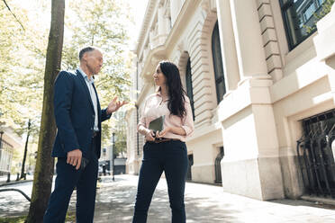 Mature businessman discussing with businesswoman on footpath - JOSEF06480