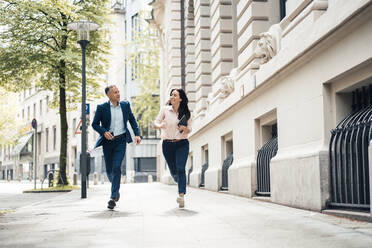 Businessman and businesswoman running on footpath in city - JOSEF06489