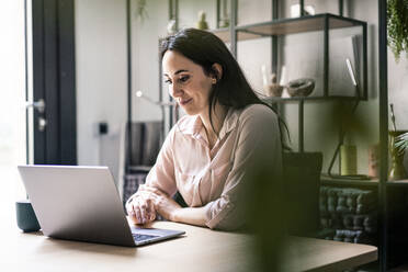 Smiling businesswoman using laptop at desk in coworking office - JOSEF06496