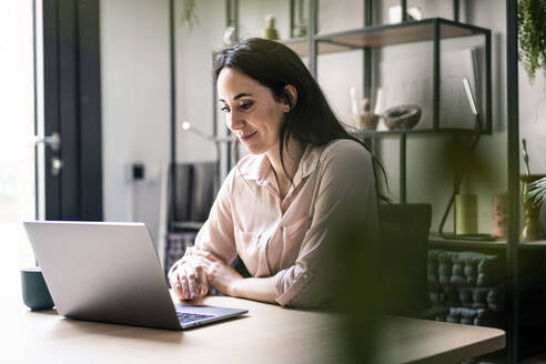 Lächelnde Geschäftsfrau mit Laptop am Schreibtisch in einem Coworking-Büro - JOSEF06496