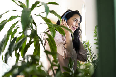 Businesswoman enjoying music through wireless headphones in coworking office - JOSEF06506