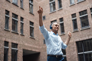 Businessman with eyes closed enjoying music and dancing in front of office building - JOSEF06526