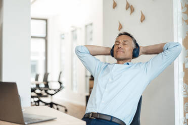 Businessman with hands behind head relaxing in office - JOSEF06532