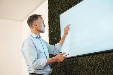 Älterer Geschäftsmann, der auf einen Touchscreen-Computermonitor in einem Coworking-Büro zeigt - JOSEF06535