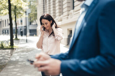 Lächelnde Geschäftsfrau, die am Fußweg mit einem Smartphone spricht - JOSEF06540