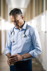 Doctor holding disposable coffee cup at corridor in hospital - JOSEF06568