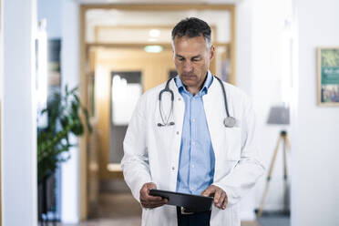 Mature doctor examining medical record on tablet PC in hospital - JOSEF06570