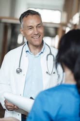 Happy doctor discussing over medical record with nurse in hospital - JOSEF06583