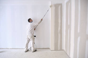 Painter painting wall with roller at construction site - AGOF00211