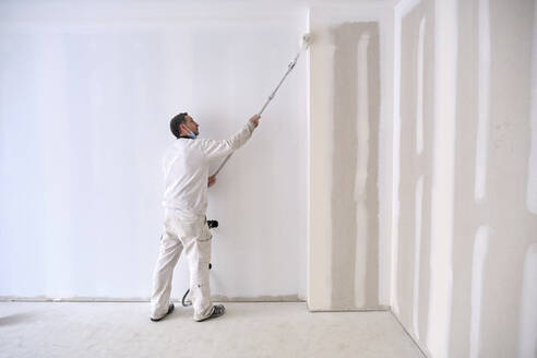 Painter painting wall with roller at construction site - AGOF00211