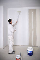 Maler auf der Baustelle, der die Wand mit einer Rolle streicht - AGOF00212