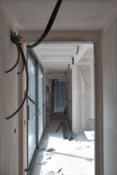 Leerer Korridor mit Kabeldrähten, gesehen durch eine Türöffnung auf einer Baustelle - AGOF00213