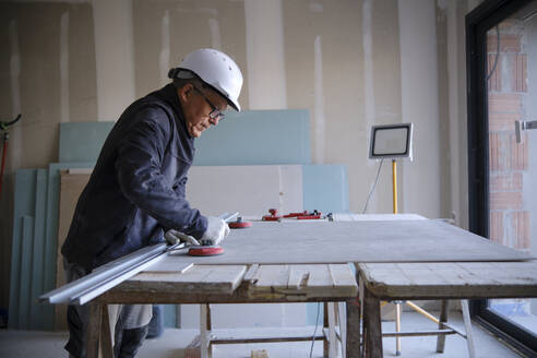 Construction worker with sheetrock on workbench at site - AGOF00216