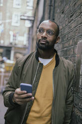 Contemplative man with smart phone leaning on wall - AMWF00085