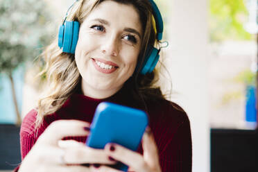 Smiling woman with smart phone listening music through headphones - AMWF00106