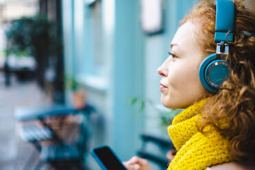 Thoughtful woman listening music through headphones - AMWF00113