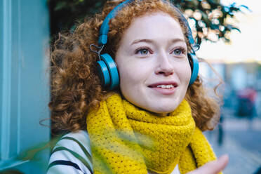 Lächelnde Frau mit gelbem Schal hört Musik über Kopfhörer - AMWF00114