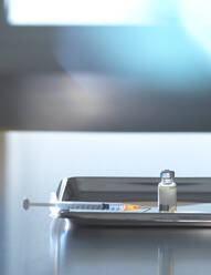 Impfstofffläschchen mit Spritze in einem Tablett auf dem Schreibtisch - ABRF00946