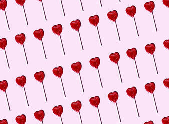 Pattern of heart shaped lollipops flat laid against pink background - EGHF00328