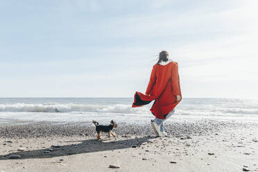 Woman with dog admiring sea at beach - OMIF00445