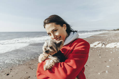 Lächelnde Frau mit Yorkshire-Terrier am Strand - OMIF00446