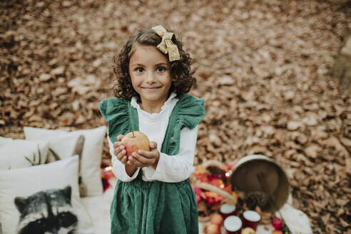 Lächelndes Mädchen mit Apfel im Wald in der Weihnachtszeit - GMLF01256