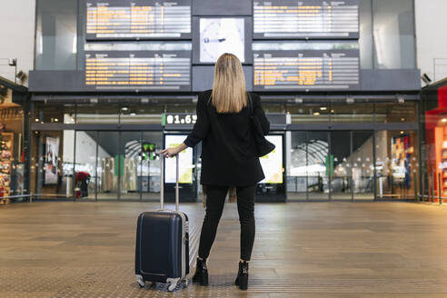 Frau schaut auf die Ankunft-Abfahrtstafel am Bahnhof - JRVF02622