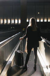 Frau mit Gepäck auf Rädern fährt auf Rolltreppe im Bahnhof - JRVF02629