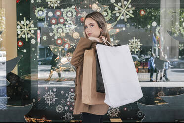 Confident woman with shopping bags by store window at Christmas - JRVF02634