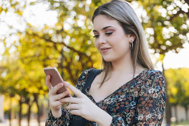 Smiling woman using smart phone in park - JRVF02657