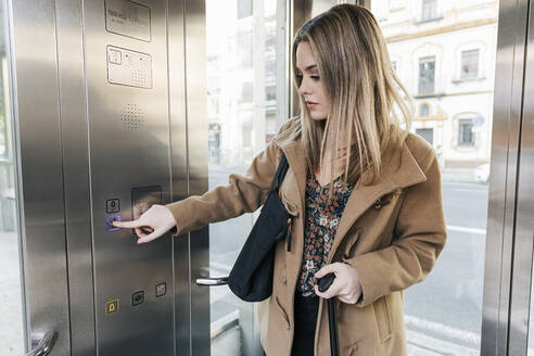 Blond woman pressing button in elevator - JRVF02659