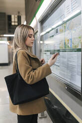 Frau mit Handtasche benutzt Smartphone in U-Bahn-Station - JRVF02664