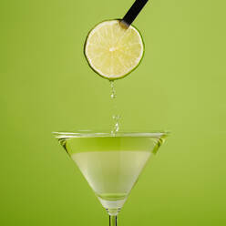 Unbekannte Person hält eine frische Limettenscheibe über einem Glas Daiquiri-Cocktail vor grünem Hintergrund - ADSF33421