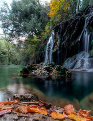 Malerischer Blick auf einen Wasserfall, der durch Felsformationen in einem üppigen grünen Wald in Katalonien in Spanien fließt - ADSF33428
