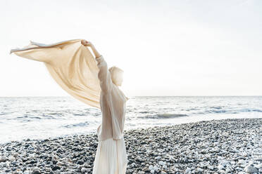 Woman holding blanket aloft at beach - OMIF00460