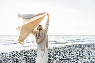 Woman holding blanket enjoying at beach - OMIF00461