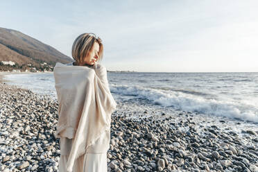 Blonde Frau in Decke eingewickelt am Strand - OMIF00464