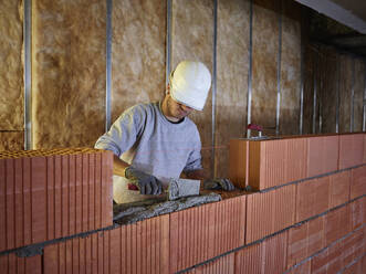 Maurer beim Auftragen von Zement auf Ziegelsteine mit Handwerkzeug auf der Baustelle - CVF01832