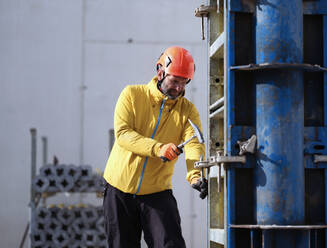 Arbeiter, der einen Nagel mit einem Hammer an einer Metallstruktur auf einer Baustelle befestigt - CVF01835