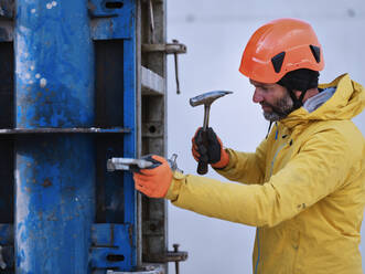 Arbeiter, der einen Nagel mit einem Hammer an einer Metallstruktur befestigt - CVF01837