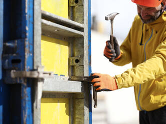 Arbeiter hämmert einen Nagel in eine Schalungswand auf der Baustelle - CVF01839