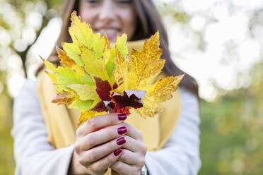 Junge Frau hält Herbstblätter im Park - EIF03148