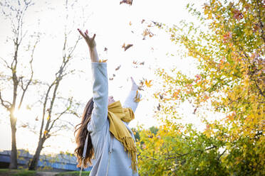 Carefree woman throwing leaves in autumn park - EIF03151