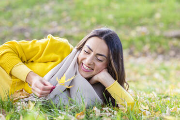 Glückliche junge Frau mit Blatt im Gras liegend im Herbst Park - EIF03159