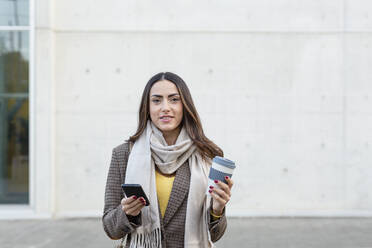 Junge Frau mit Smartphone und wiederverwendbarem Kaffeebecher auf dem Fußweg - EIF03172